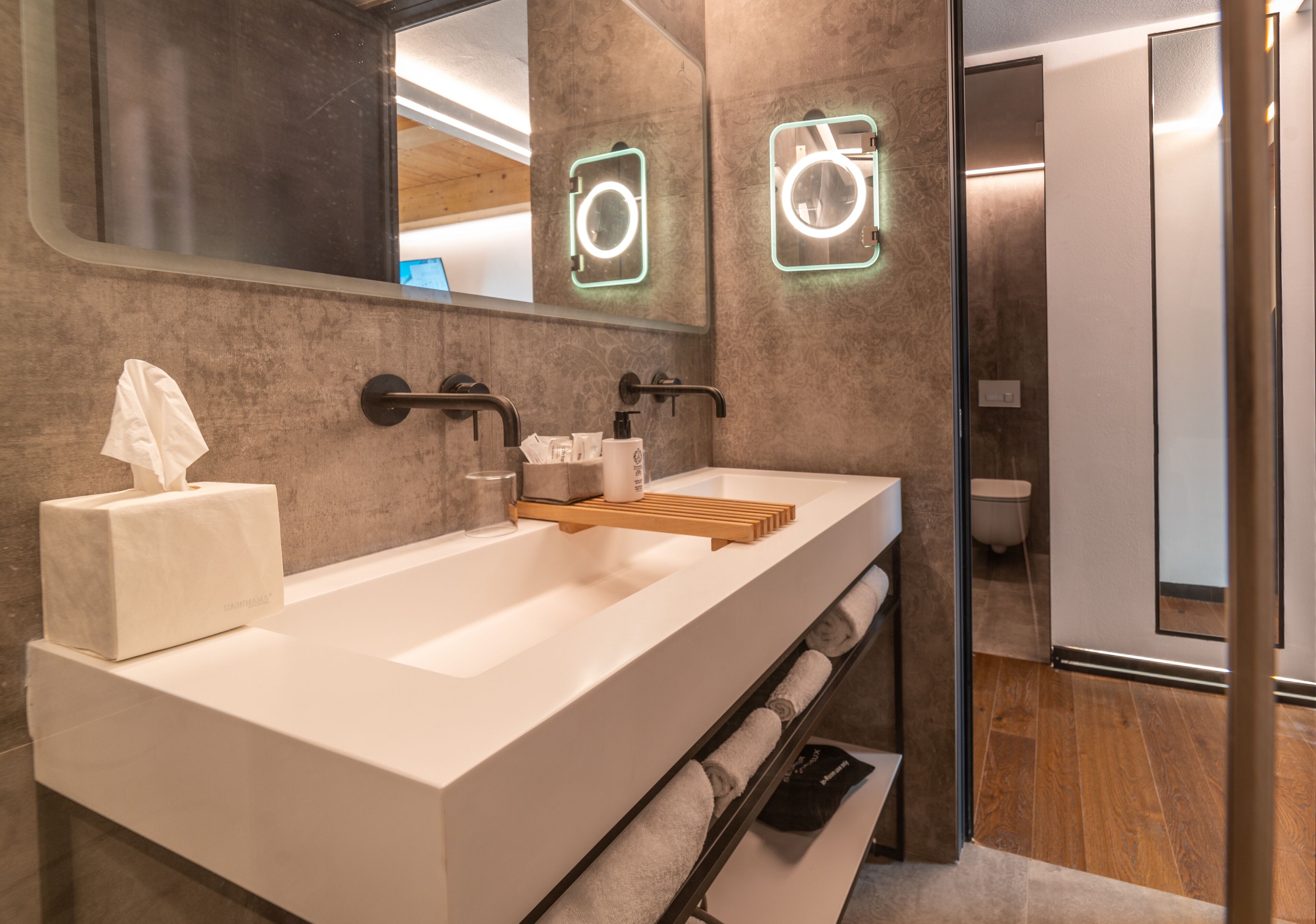 Un baño moderno con un espejo grande, un lavabo blanco y un estante de madera.
