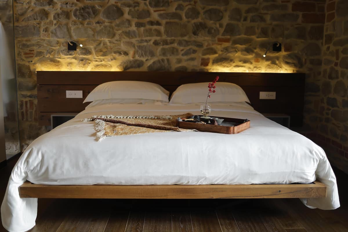 A bed with white linens, a wooden headboard, and a stone wall backdrop.