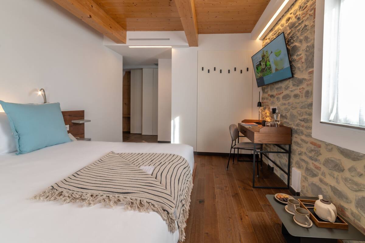 A bedroom with a bed, a desk, and a stone wall.