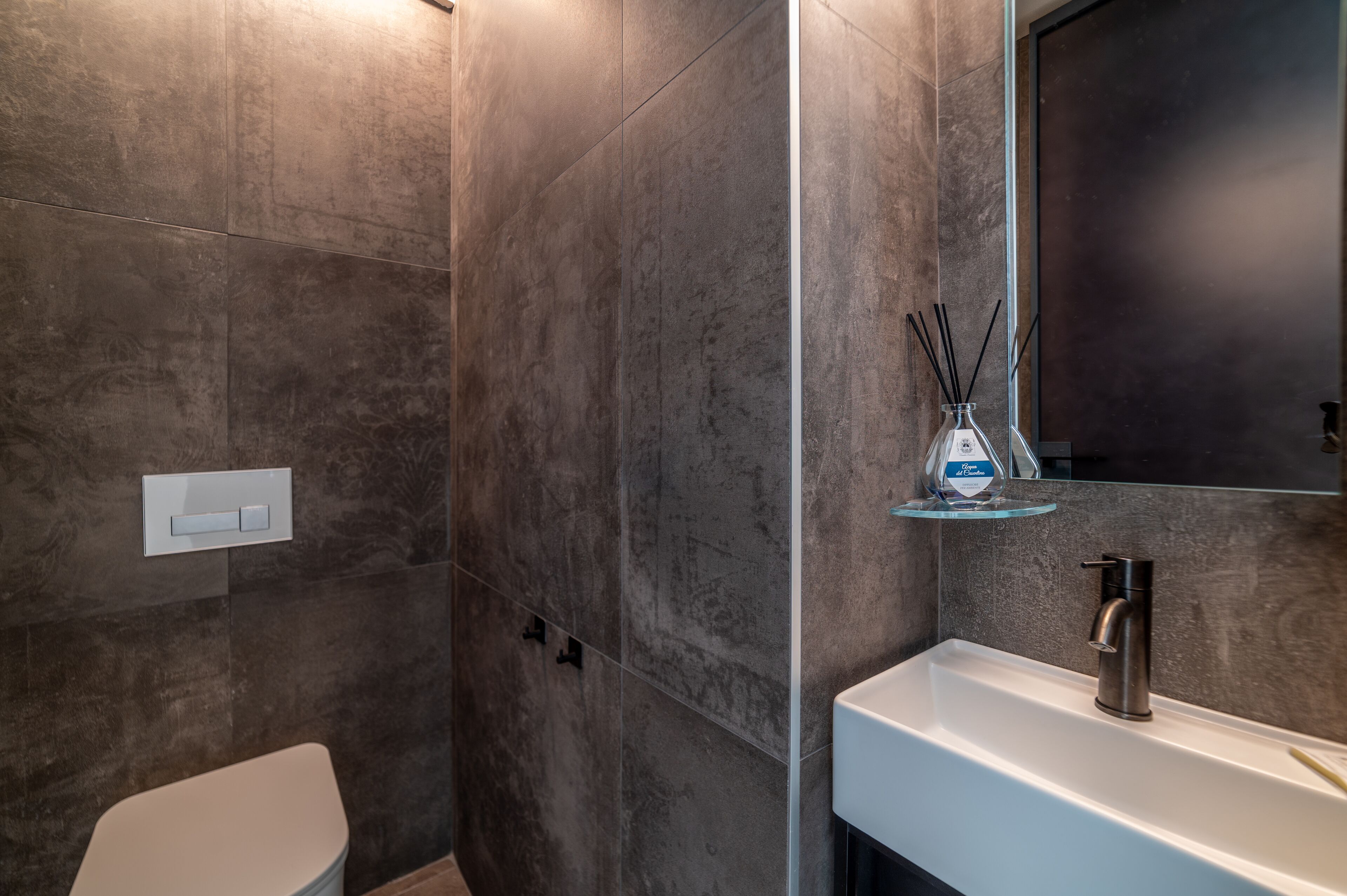 A modern bathroom with a white sink, a glass shelf with a bottle, and a large mirror.