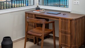 A corner room with a wooden desk, a chair, and a view of the sea through large windows.