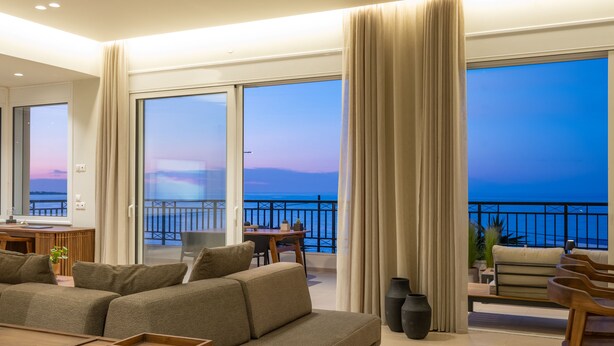 A spacious living area with a large sofa, a wooden coffee table, and a balcony with a view of the sea.
