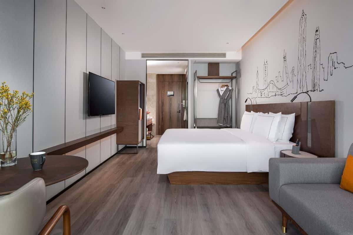 Ein modernes Hotelzimmer mit Bett, Fernseher, Sitzecke und Stadtbild an der Wand.