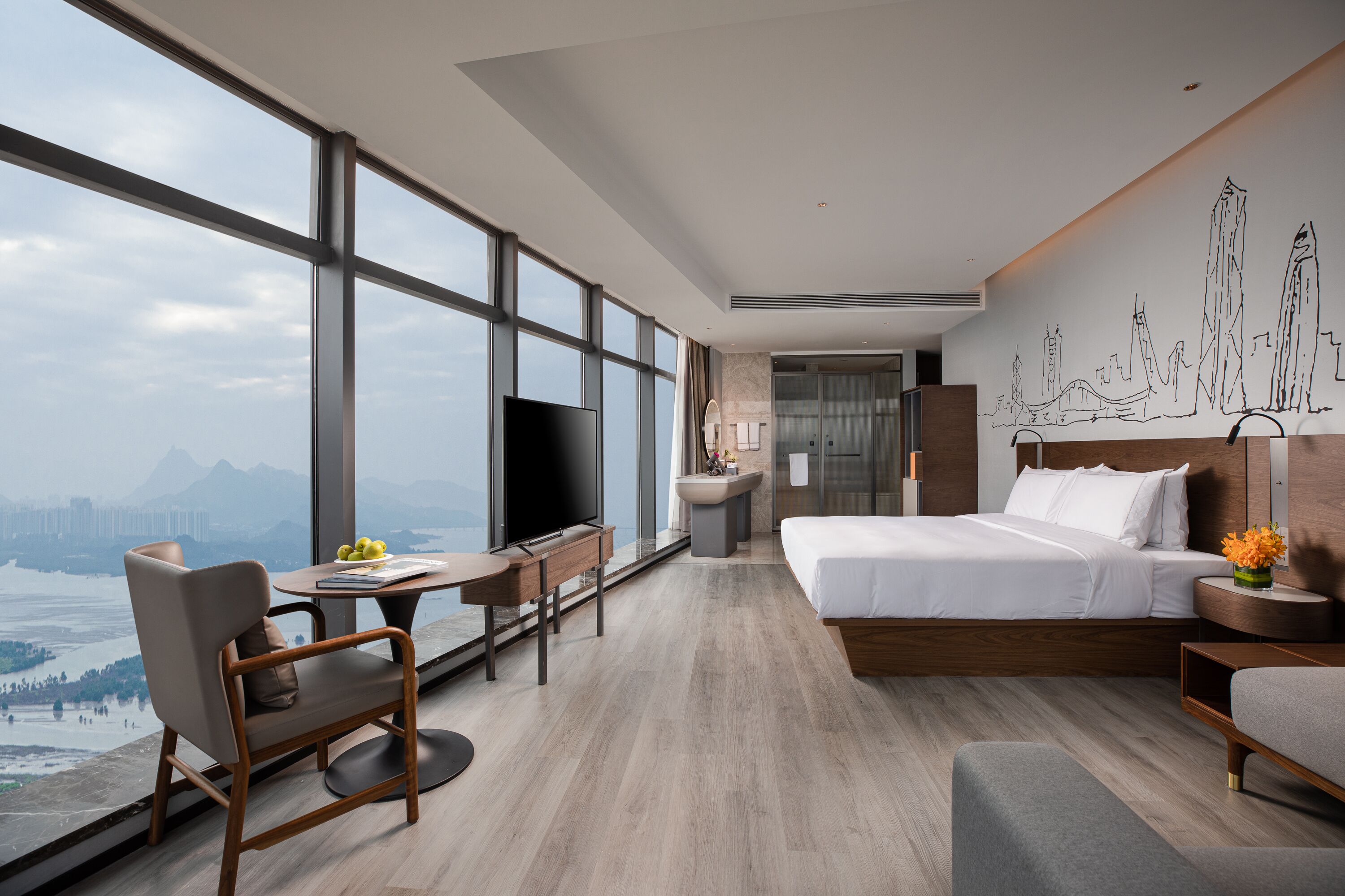 A modern hotel room with a large window, a bed, a desk, and a chair.