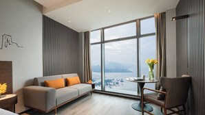 Ein modernes Hotelzimmer mit großem Fenster, einer Couch, einem Sessel und einem kleinen Tisch mit Blumenvase.