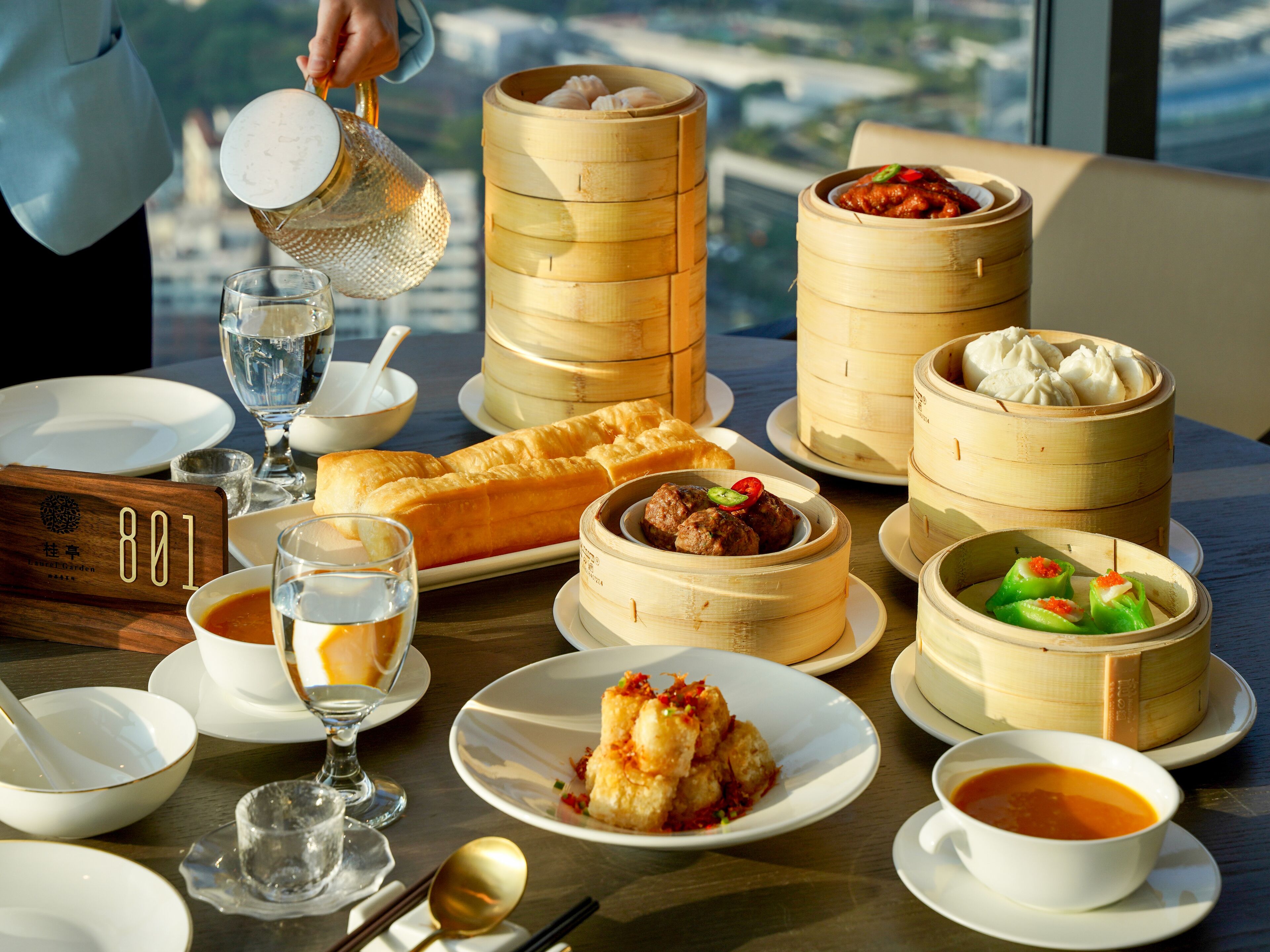 A table set with various dishes, including dumplings and a bread roll, in a restaurant with a view of the city.