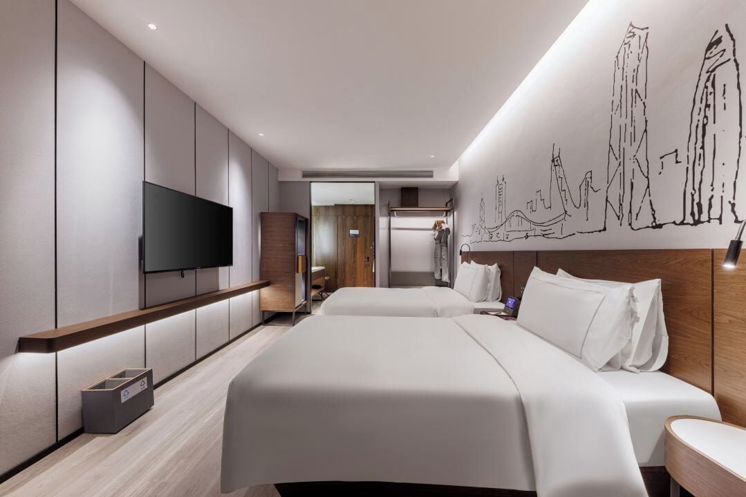 A modern hotel room with a large bed, a TV, a wooden headboard, and a wall mural.