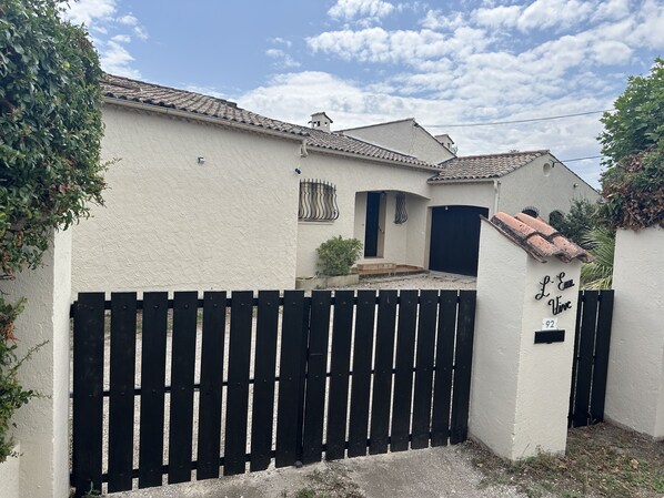 A white building with a black gate, a tiled roof, and a sign reading "L'Eau Vive".