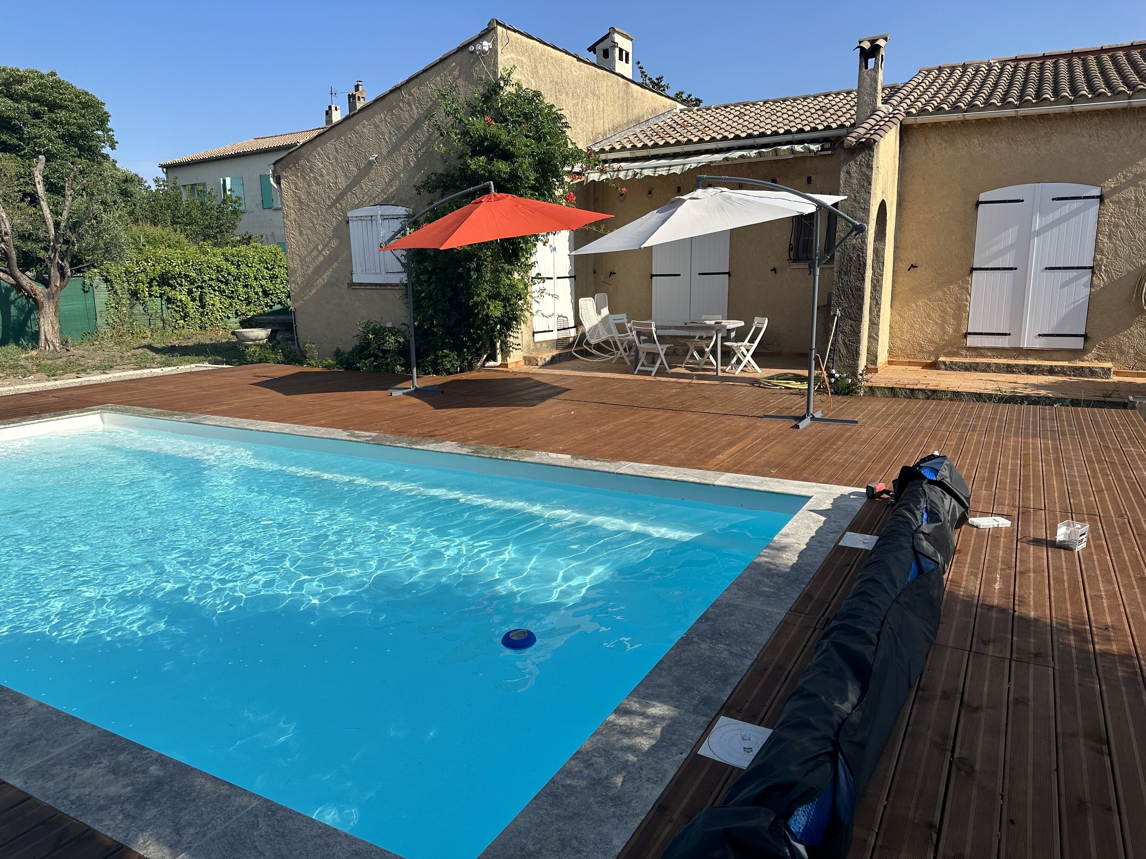 A swimming pool with a wooden deck, outdoor furniture, and a building with a tiled roof.