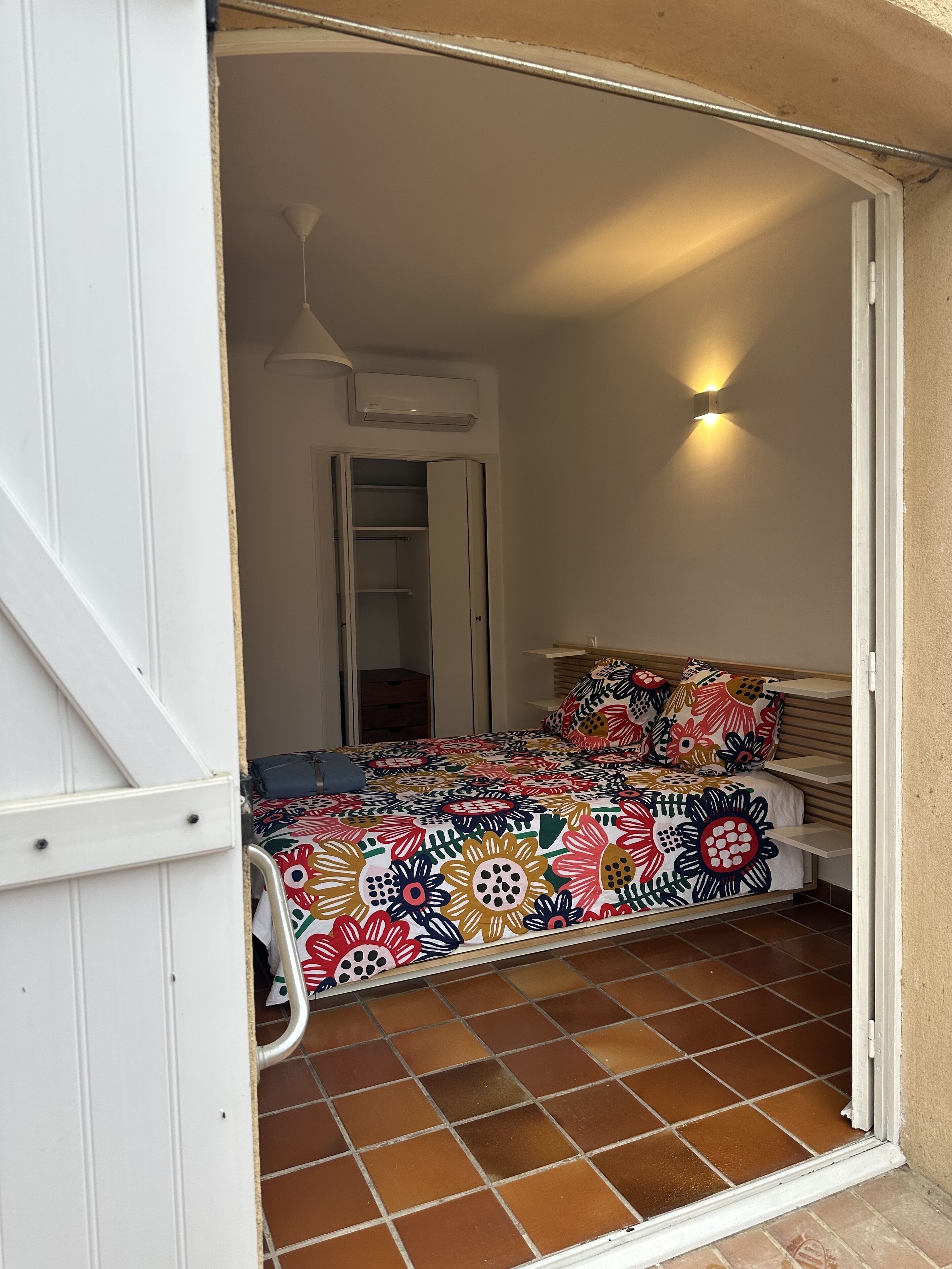 A bedroom with a colorful floral bedspread, a white wardrobe, and a ceiling fan.