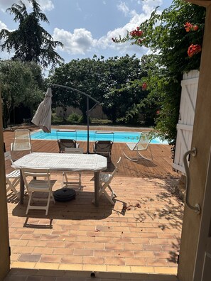 An outdoor patio with a table and chairs, a pool, and a wooden deck.