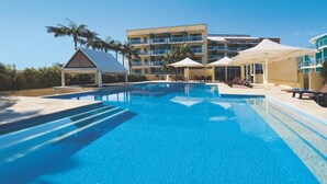 A swimming pool with lounge chairs and umbrellas, surrounded by a building with multiple balconies.