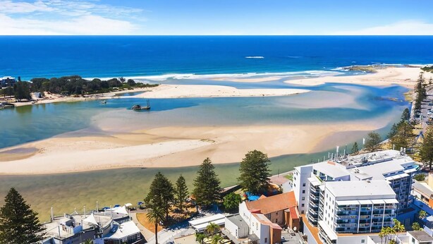 A coastal area with clear waters, sandy beaches, and buildings with balconies overlooking the sea.