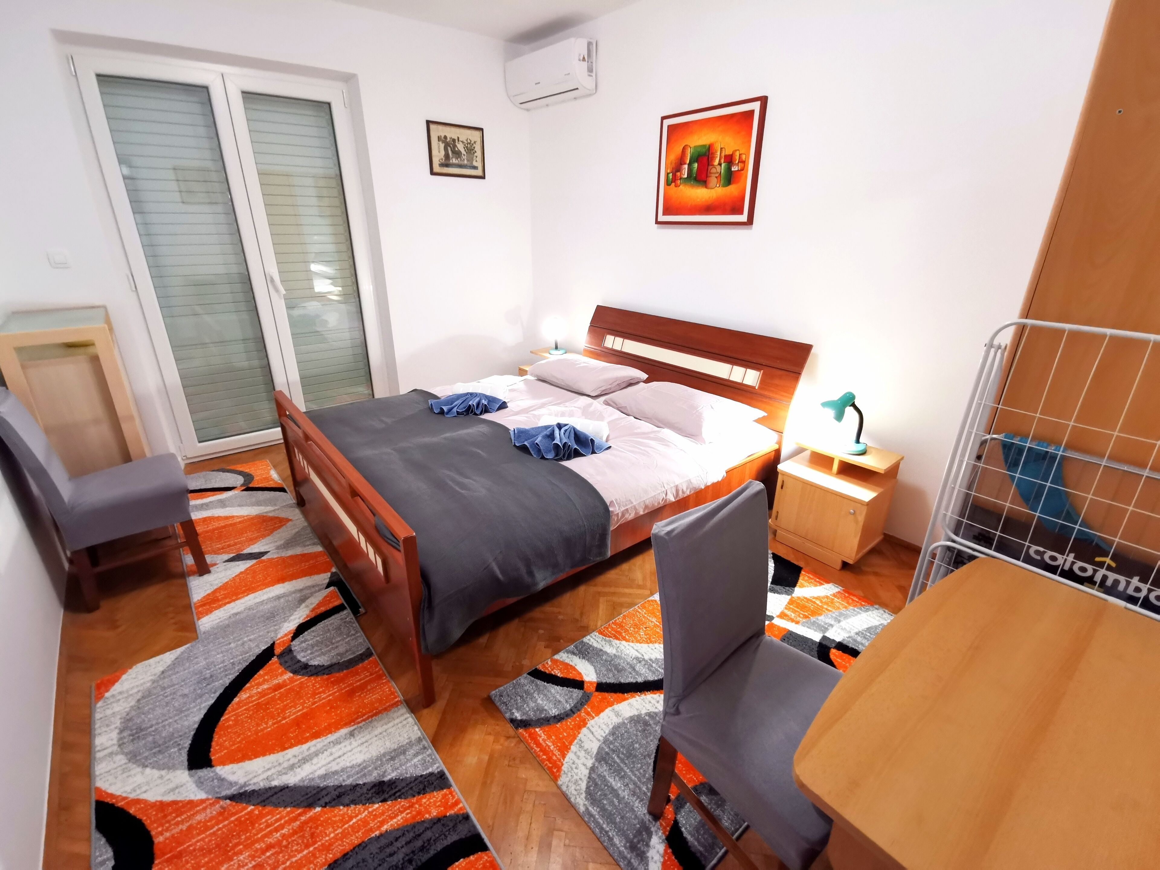 A bedroom with a bed, a desk, a chair, a nightstand, and a radiator.