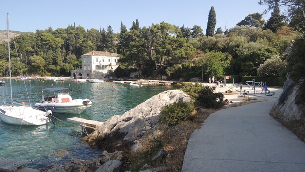 Un port de plaisance situé sur la côte, avec des bateaux, un bâtiment blanc et un sentier piétonnier.