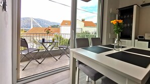 Un balcon avec une table et des chaises, un vase rempli de fleurs et une vue sur des bâtiments et des montagnes.