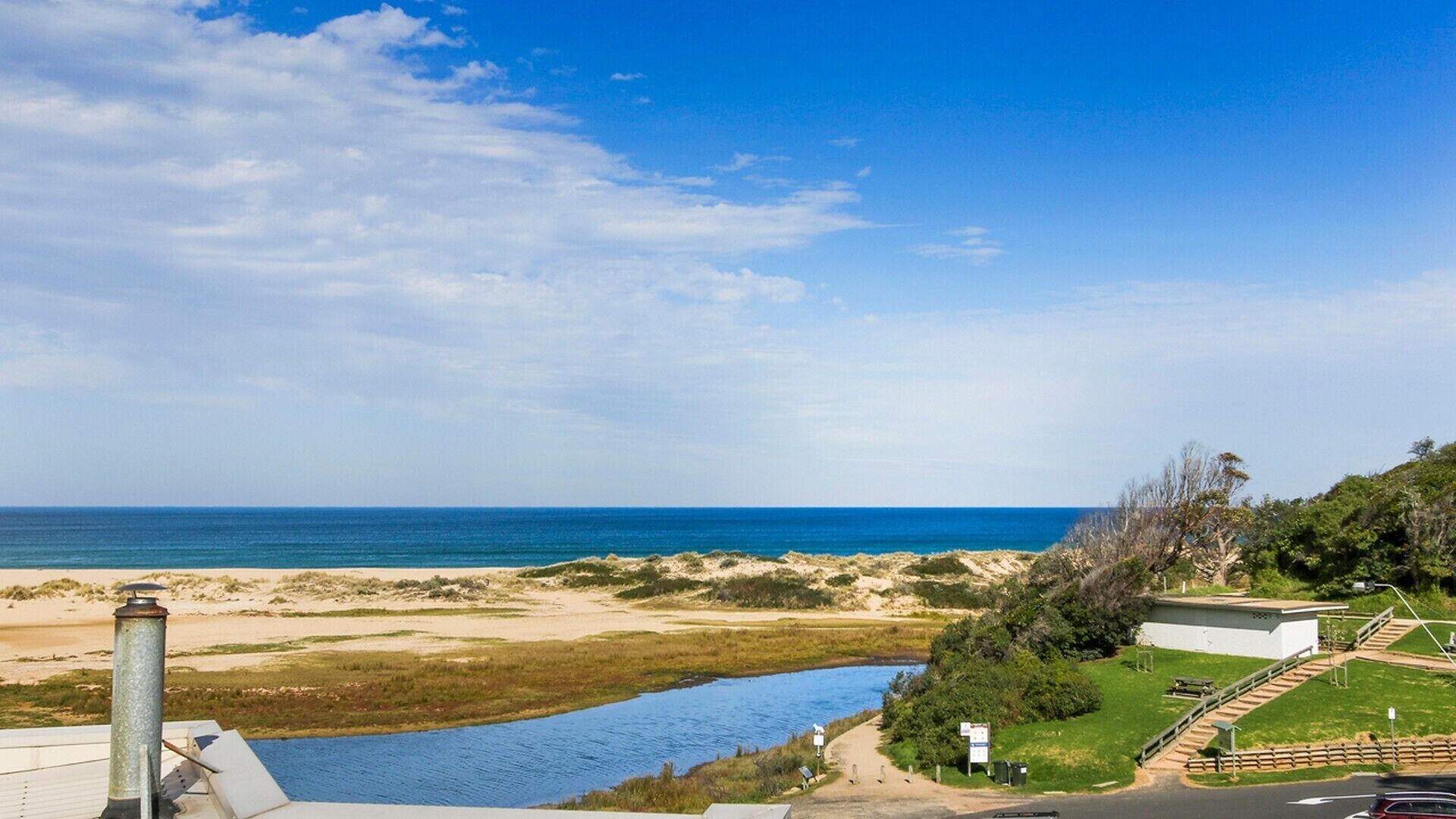 Un paysage côtier comprenant une plage, une rivière et une route avec un bâtiment situé sur une colline.