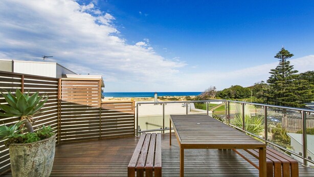 Terraza de madera con mesa y bancos con vistas a una playa.