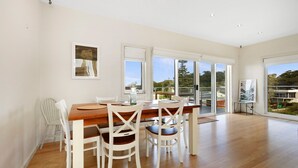 Comedor con mesa de madera y sillas blancas, ventanas amplias y vistas al exterior.