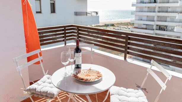 A balcony with a round table, two chairs, a wine bottle, and a plate of food. - Apartamento Nuevo Junto a la Playa Vistas al mar (Punta Umbria)