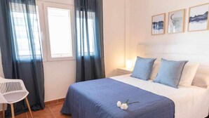 A bedroom with a bed, a chair, and a window with curtains. - Apartamento Nuevo Junto a la Playa Vistas al mar (Punta Umbria)