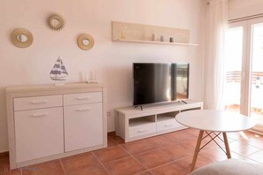 A living room with a TV, a white cabinet, a small table, and decorative wall art.