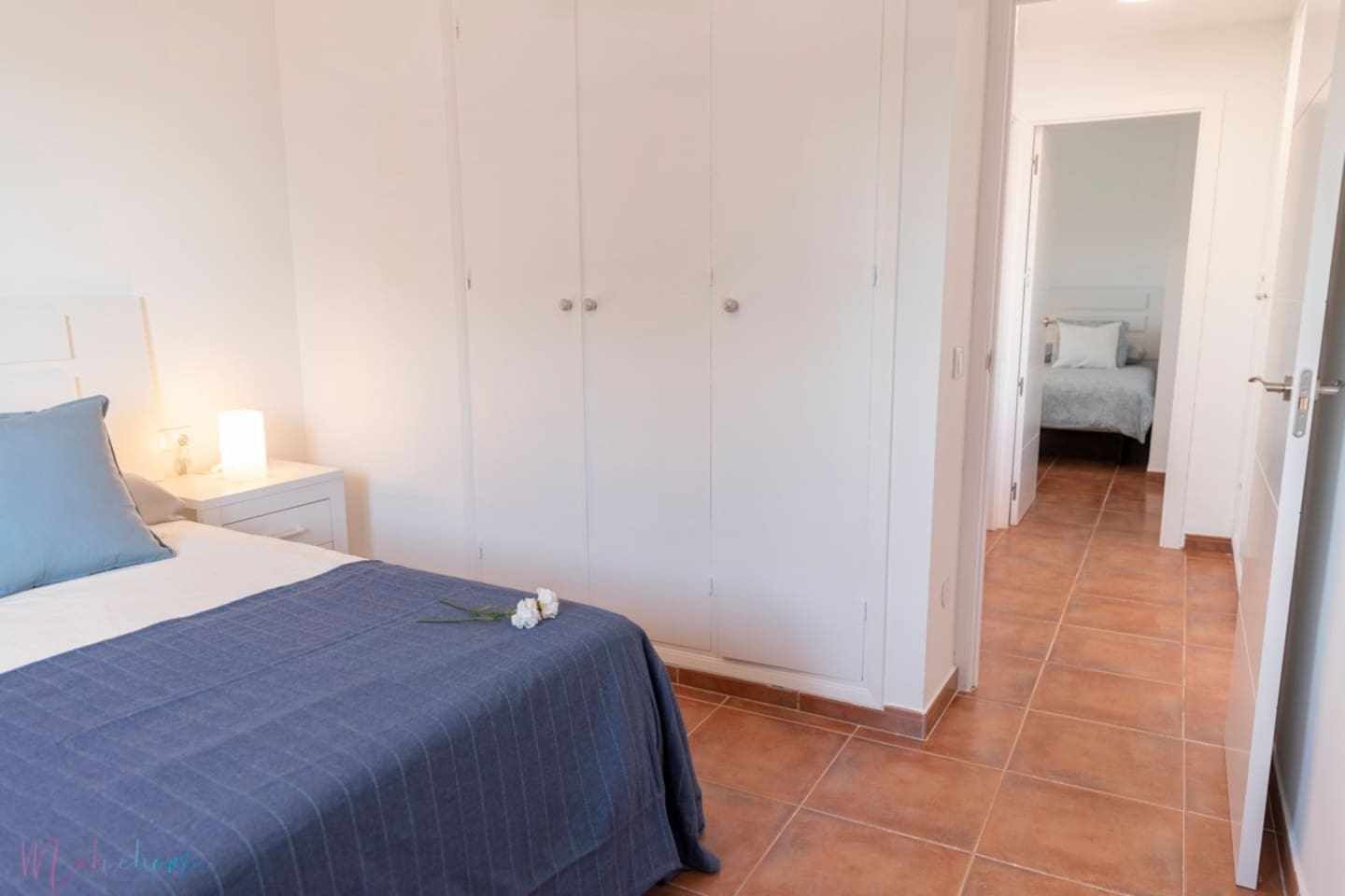 Un dormitorio con cama, mesita de noche, armario y baño visible a través de una puerta abierta.