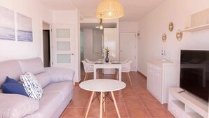 A modern living room with a sofa, a dining table, and a TV. - Apartamento Nuevo Junto a la Playa Vistas al mar (Punta Umbria)