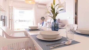 A dining area with a table set for two, a vase with flowers, and a view of the outdoors. - Apartamento Nuevo Junto a la Playa Vistas al mar (Punta Umbria)