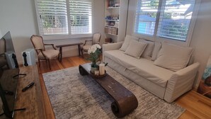 Una sala de estar con un sofá, una mesa de centro con una planta, un televisor y una estantería.