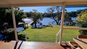 Una terraza de madera con una mesa y sillas, con vistas a un lago con barcos y árboles.