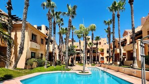 A swimming pool surrounded by palm trees and beige buildings.