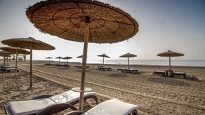 A beach with rows of sun loungers and thatched umbrellas.