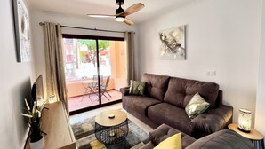 A living room with a brown sofa, a round coffee table, a ceiling fan, and a large window with curtains.