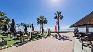 An outdoor seating area with tables and chairs, palm trees, and a clear view of the beach.