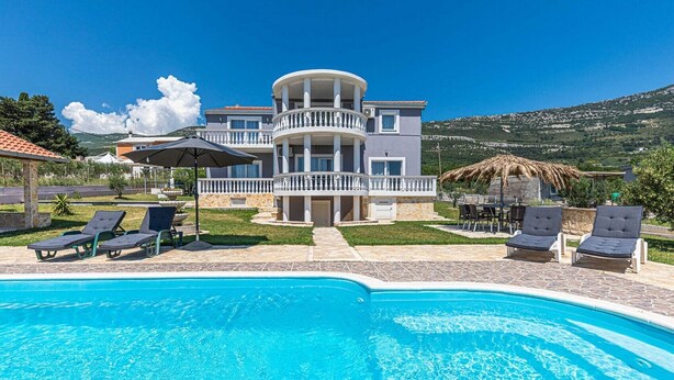 Una casa de dos plantas con piscina, mobiliario exterior y vistas a las colinas.