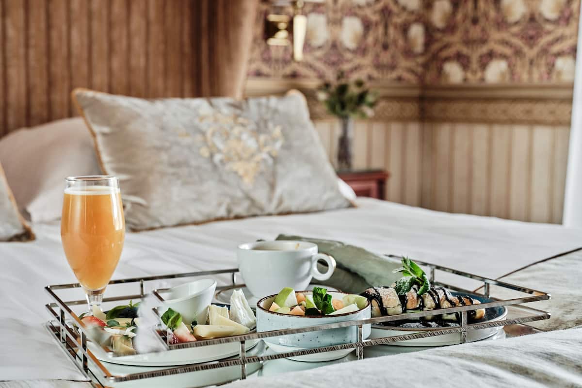 Ein ordentlich angerichtetes Frühstücksbrett mit verschiedenen Speisen und einem Glas Orangensaft auf einem Bett.