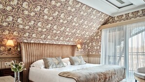 Een slaapkamer met een groot bed, een hoofdbord, twee bedlampjes, een nachtkastje en een vaas met bloemen.
