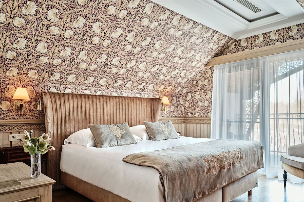 Ein Schlafzimmer mit einem großen Bett, einem Kopfteil, Nachttischlampen, einem Nachttisch und einem Fenster mit Vorhängen.