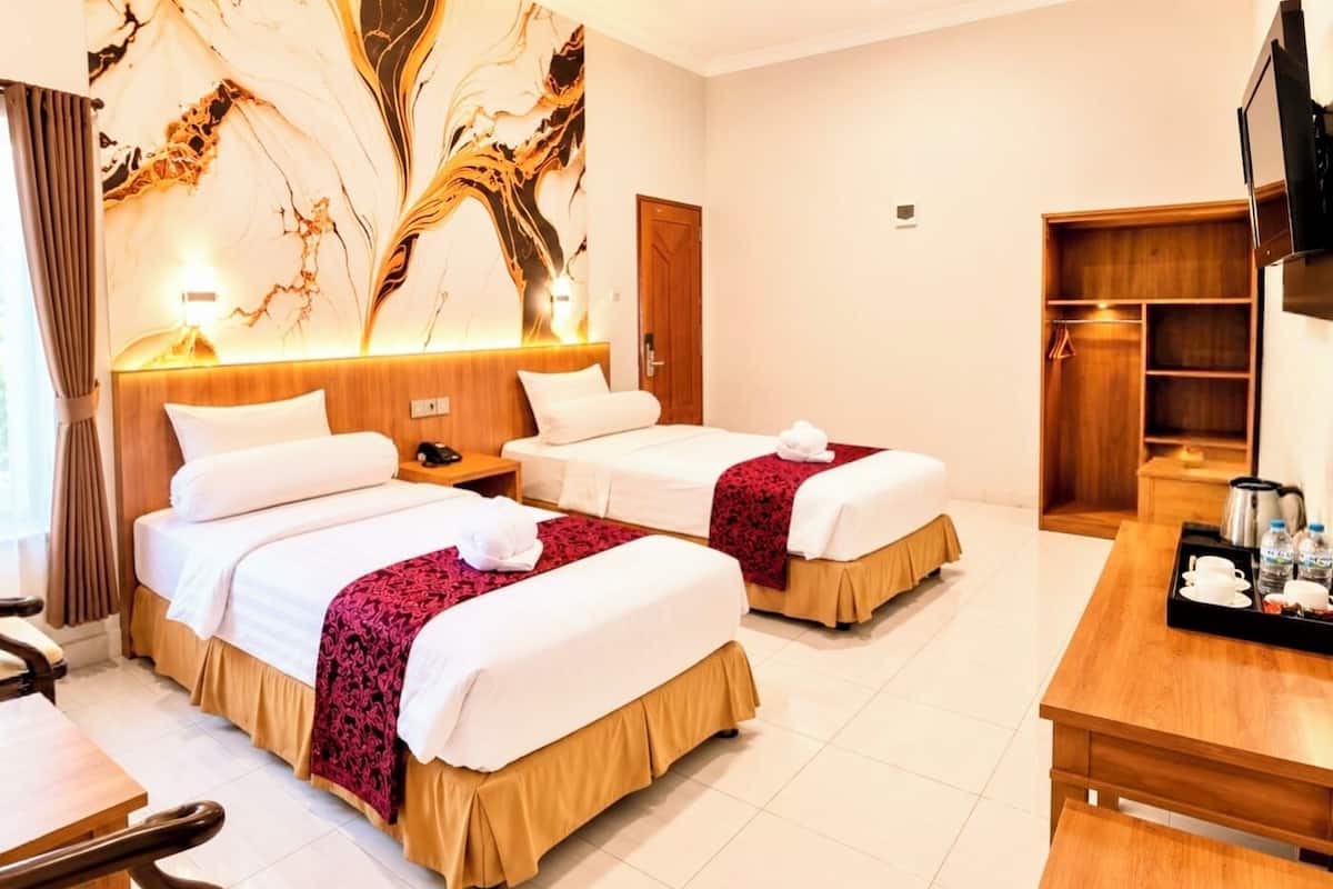 A hotel room with two beds, a wooden headboard, a TV, a desk with a tray of amenities, and a marble wall.