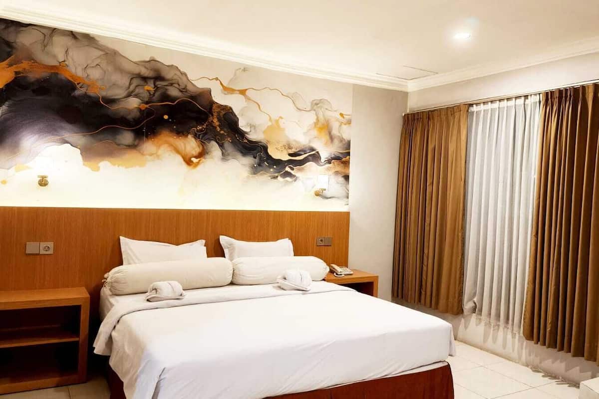 A hotel room with a large bed, a wooden headboard, a nightstand, a wall art piece, and a window with curtains.