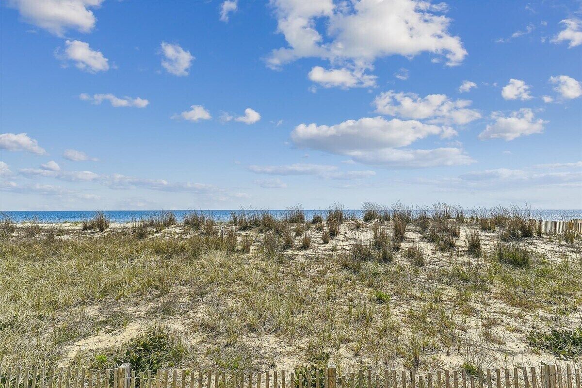 A beach with sand dunes and a wooden fence in the foreground.