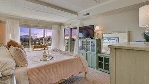 Un dormitorio con una cama grande, televisión, armario y vistas a la playa.