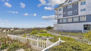 Un edificio de varios pisos con un balcón, un jardín cercado y vista a la playa.