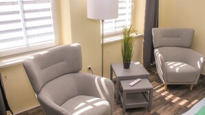 Una habitación con dos sillones grises, una mesita de noche con una lámpara y una planta en maceta.
