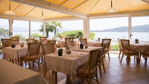 Restaurante con mesas dispuestas para comer, con vistas a un cuerpo de agua y colinas.