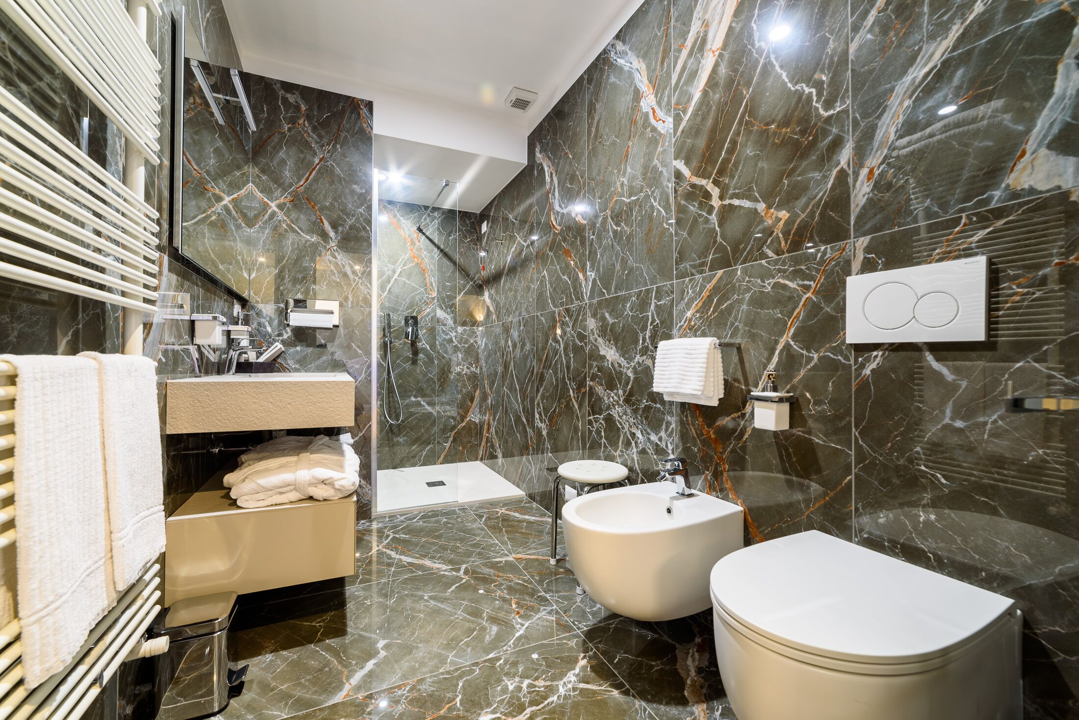 A modern bathroom with marble walls, a vanity, a bathtub, and a toilet.