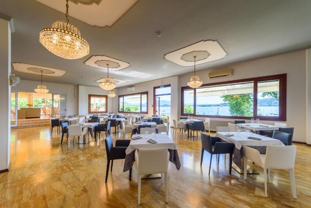 Un'ampia sala da pranzo con diversi tavoli e sedie, ampie finestre che offrono vista sull'esterno e lampadari decorativi.