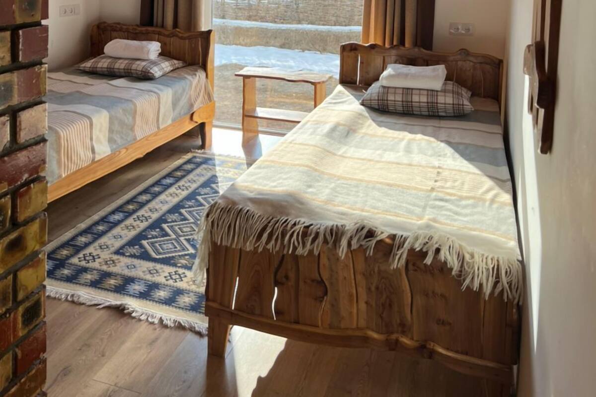 A cozy room with two wooden beds, a small table, and a view of a snowy landscape through a window.