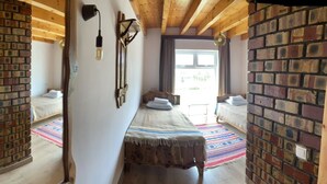 Een knus ingerichte kamer met een bakstenen muur, een bed met een kleurrijk dekbed en een houten plafond.